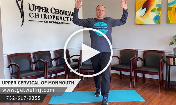 Man doing an arm stretch on exercise mat in waiting room of Upper Cervical of Monmouth NJ