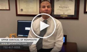 Doctor leaning against desk in office at Upper Cervical Chiropractic of Monmouth and talking
