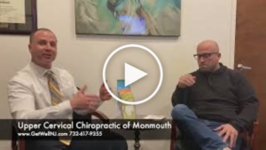 Nicely dressed man talking and sitting next to another man in chairs at Upper Cervical Chiropractic of Monmouth